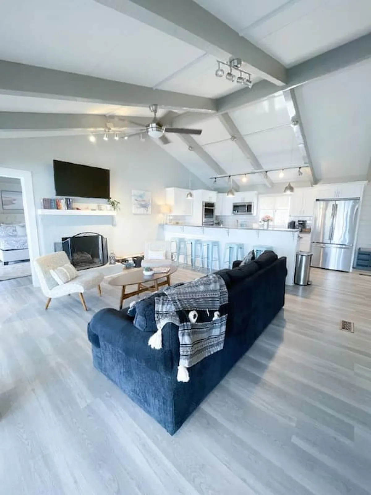 A cozy, inviting interior featuring a sofa, coffee table, fireplace, kitchen island, and a television. The layout is open and perfect for both relaxing and socializing, with views stretching from the living area to the kitchen.