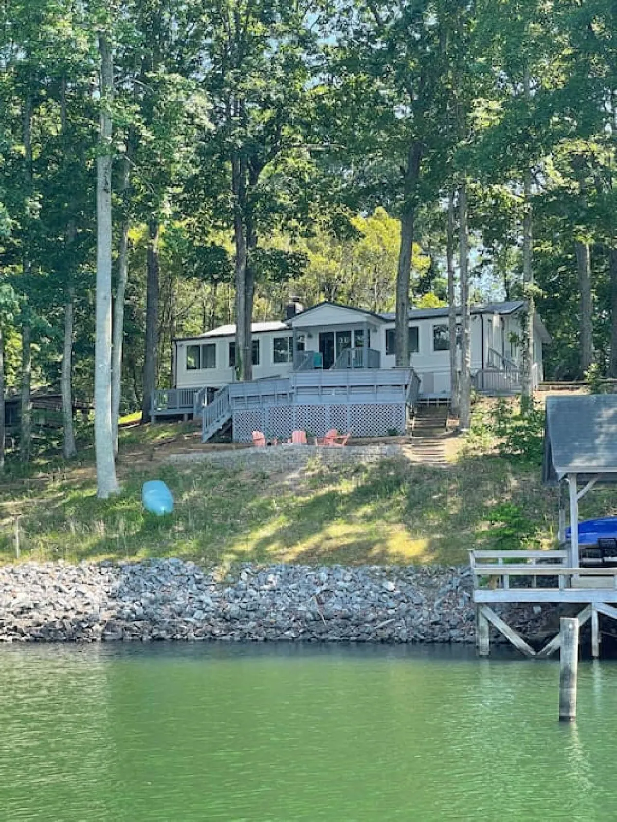 This serene exterior shot displays the cabin with its expansive deck, Adirondack chairs, and direct waterfront access surrounded by trees. The image evokes a sense of togetherness, relaxation, and connection with nature.