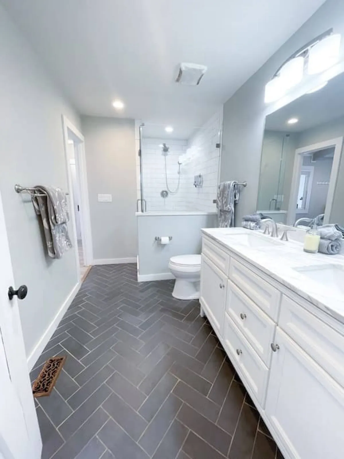 A modern bathroom with a marble-topped vanity, spacious shower area, and stylish herringbone tile flooring. The room is bright, clean, and spa-like, ideal for self-care routines.