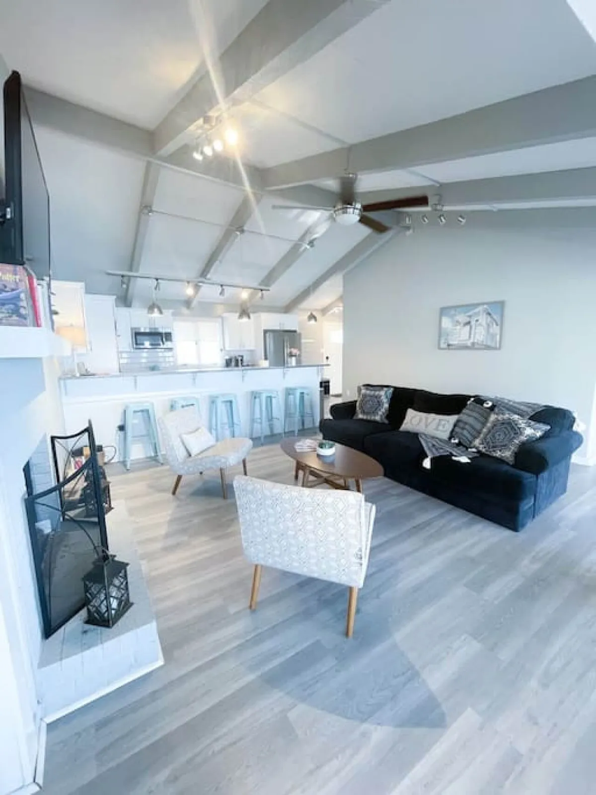A cozy living space featuring a black sofa, wooden coffee table, patterned armchairs, and a kitchen bar area. The environment is warm and inviting, ideal for relaxing, socializing, or enjoying quiet moments, with decor that signals comfort and thoughtful design.