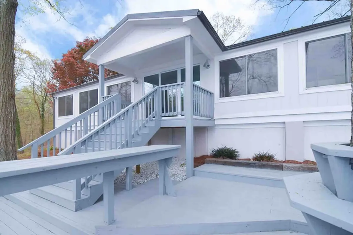 The property’s exterior showcases a staircase leading to the entrance, large windows that invite in natural light, and a spacious deck with ample seating—ideal for outdoor gatherings and quiet moments alike.