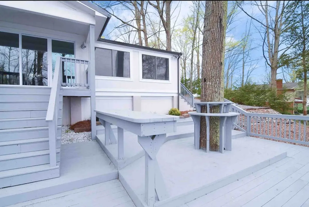 A wide view of the home's deck area, framed by a large tree and generous windows, with ample space for outdoor socializing and gatherings. The setting is bathed in soft, natural light, suggesting both daytime and evening possibilities for group activities.